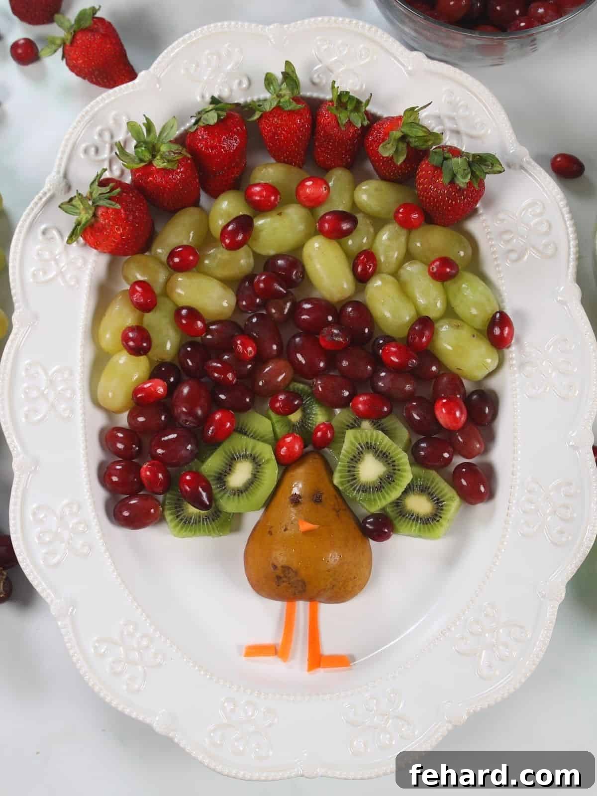 A vibrant and festive fruit platter arranged to resemble a turkey with a pear body and colorful fruit feathers, perfect for a Thanksgiving appetizer.