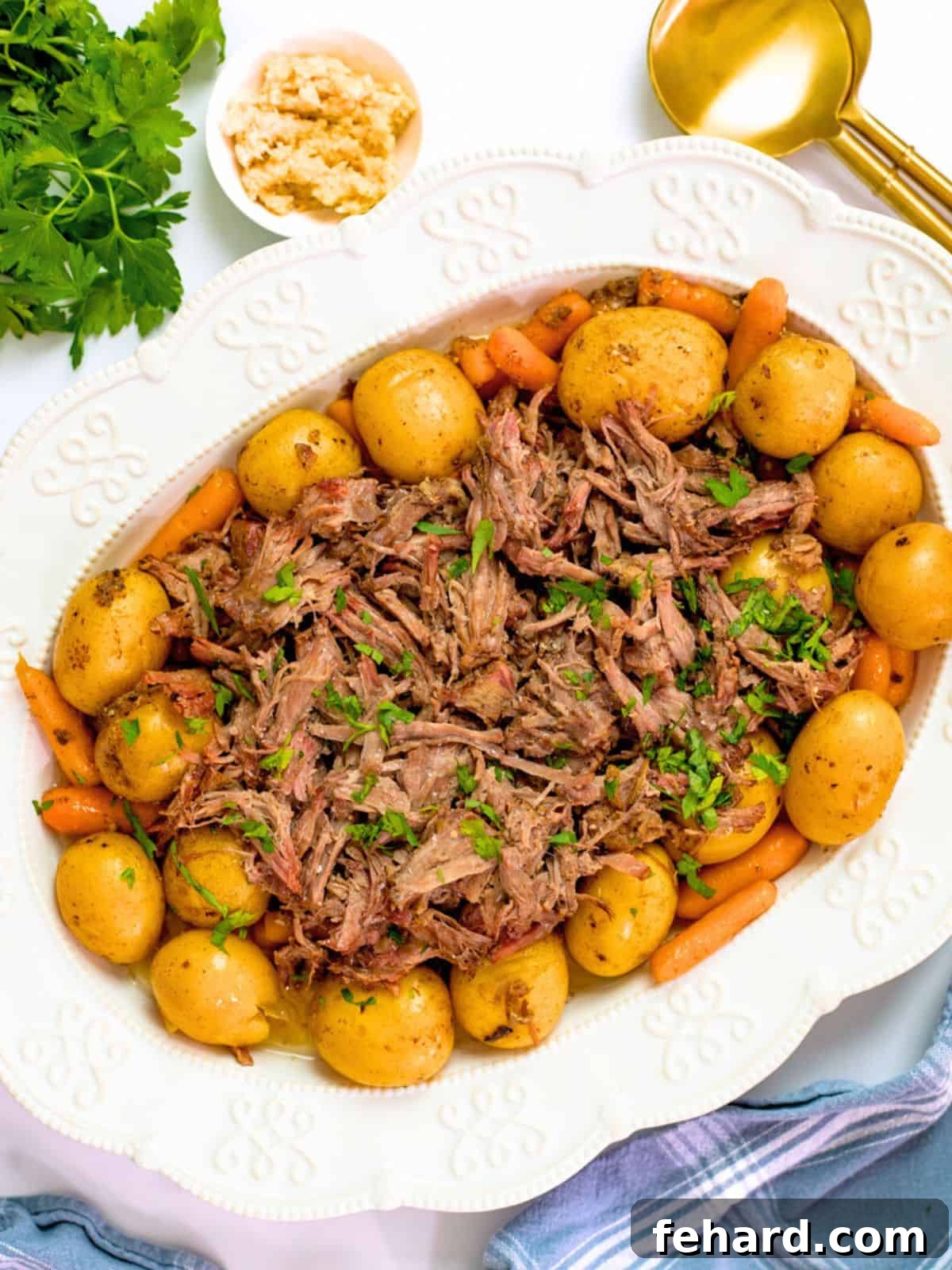 A beautifully presented crockpot roast with potatoes and carrots on a white platter, accompanied by a slow cooker, fresh horseradish, and elegant gold serving spoons.