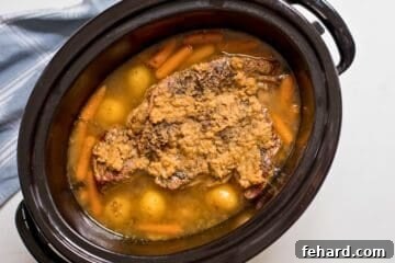 Slow cooked chuck roast in slow cooker with beef broth, baby potatoes, and baby carrots.