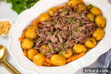 Shredded slow cooker roast on white platter dish over potatoes and carrots next to crock pot, horseradish, and gold serving spoons.