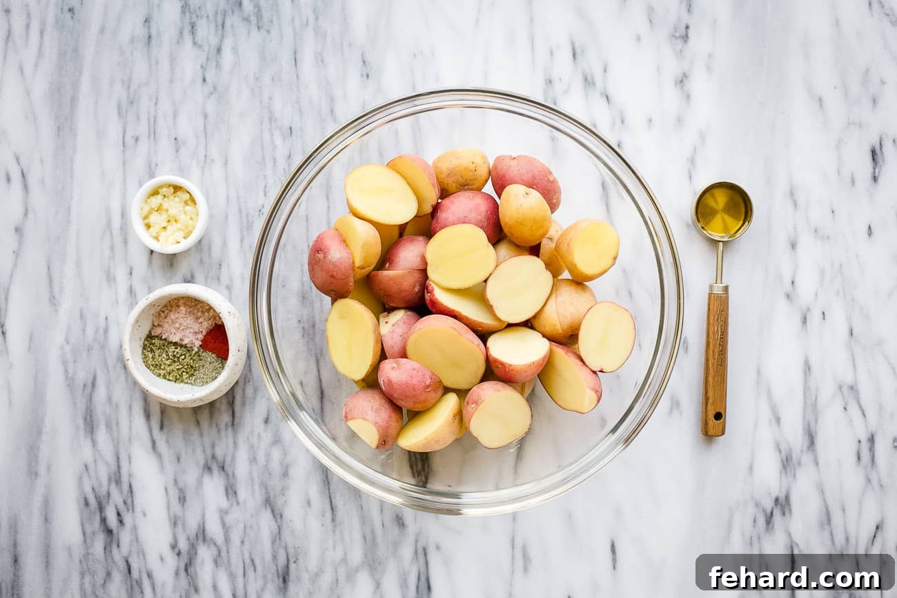 A clean, overhead shot showcasing the fresh ingredients required for air fryer baby potatoes: colorful baby potatoes, a small bowl of olive oil, and separate small piles of paprika, oregano, salt, and black pepper on a light surface.