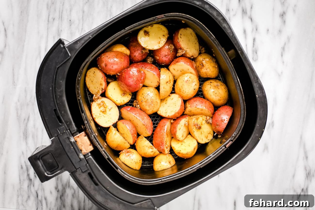 Seasoned baby potatoes, halved and spread evenly in a single layer across the air fryer basket, showing their readiness for cooking and crisping.
