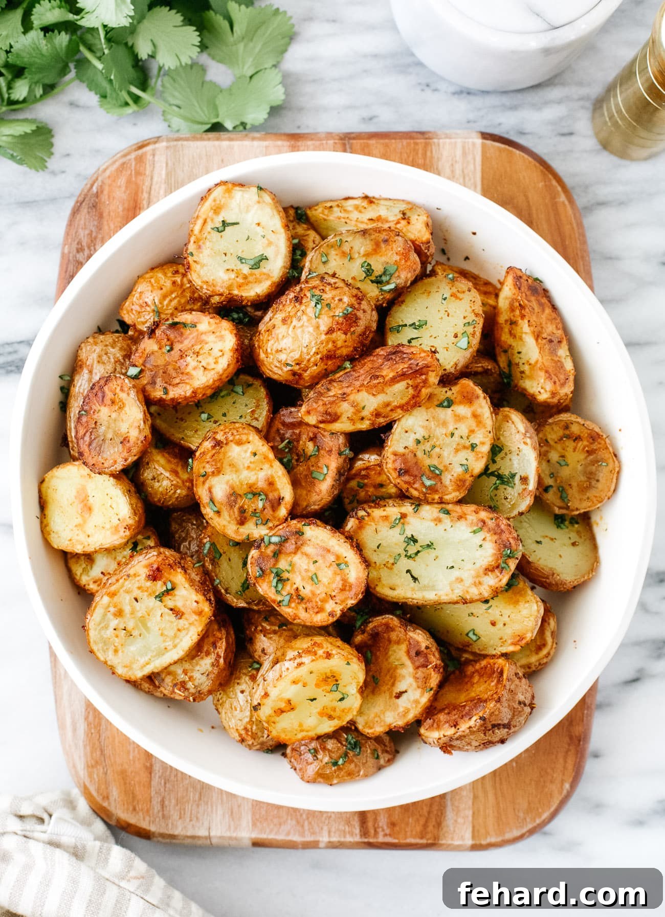 A charming close-up of a small, rustic white bowl filled with air-fried baby potatoes, garnished with fresh herbs, ready for serving.