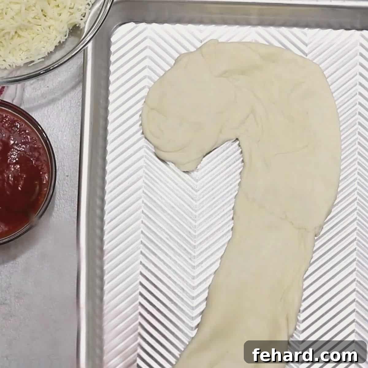 Pizza dough perfectly shaped like a candy cane on a baking sheet, ready for toppings.