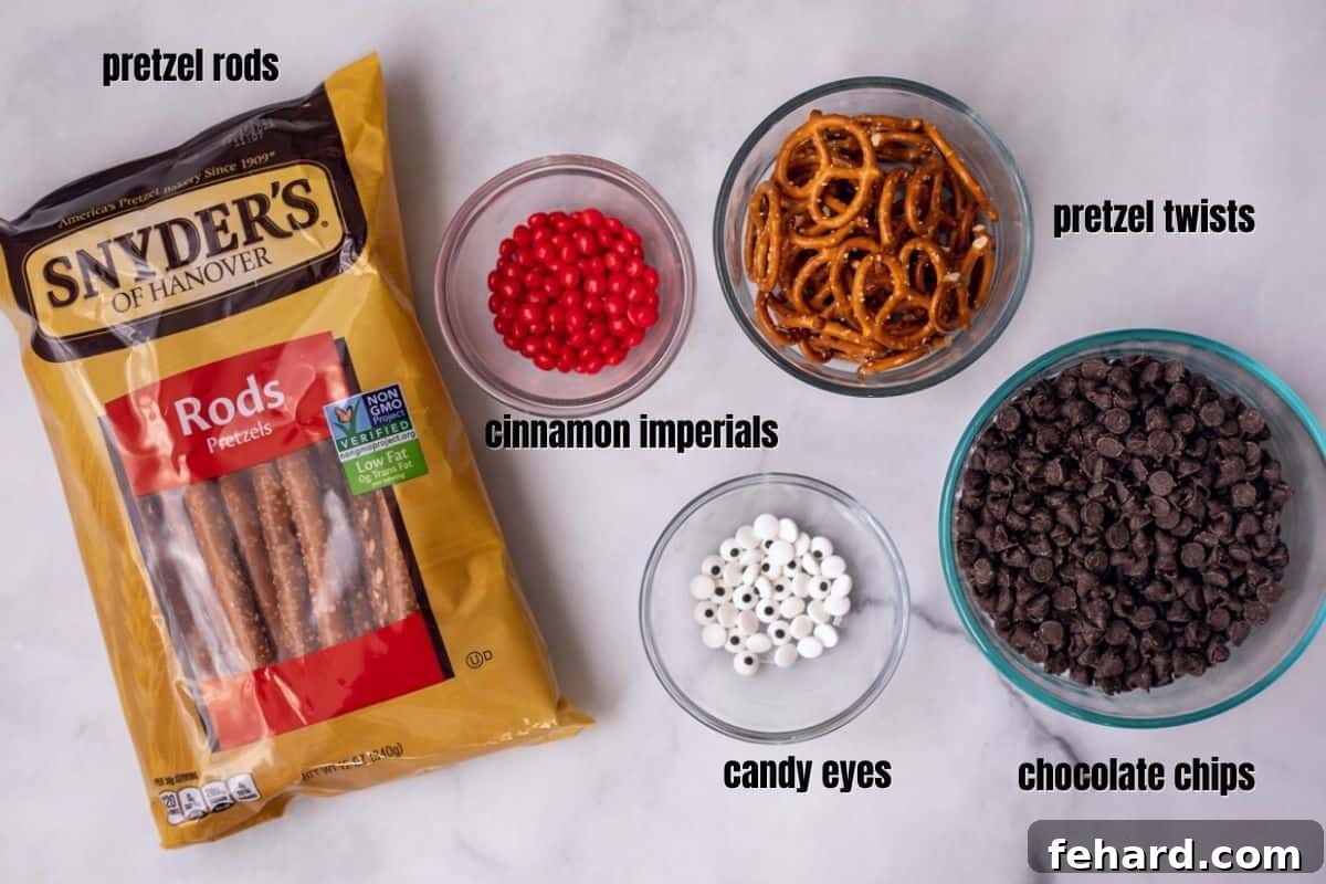 Key ingredients for making reindeer pretzels artfully arranged on a white kitchen counter, including chocolate chips, pretzel rods, pretzel twists, candy eyes, and a small bowl of red cinnamon imperials.