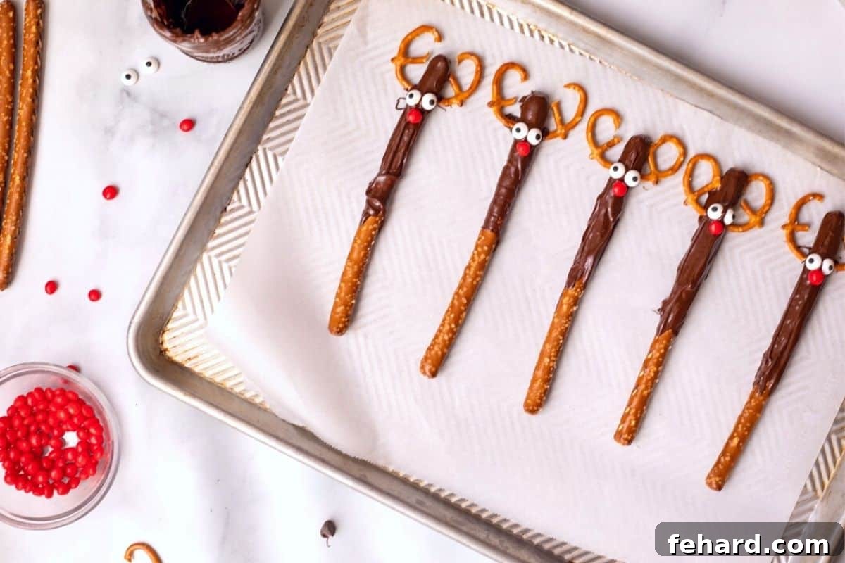 Assembled Rudolph Chocolate Covered Pretzels meticulously laid out on a parchment paper-lined baking sheet, awaiting the final hardening process.
