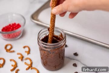 Pretzel rod being dipped halfway into jar of melted chocolate.