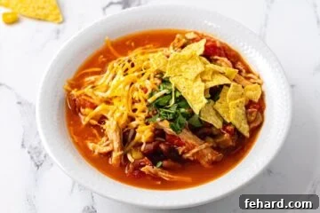 Bowl of chicken chili in white bowl topped with shredded cheese and chips.