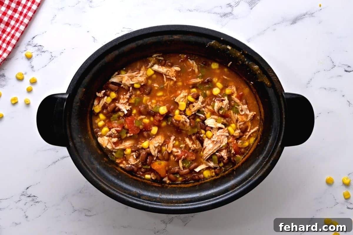 Crockpot with cooked chicken chili made with shredded chicken, beans, corn, and taco seasoning.