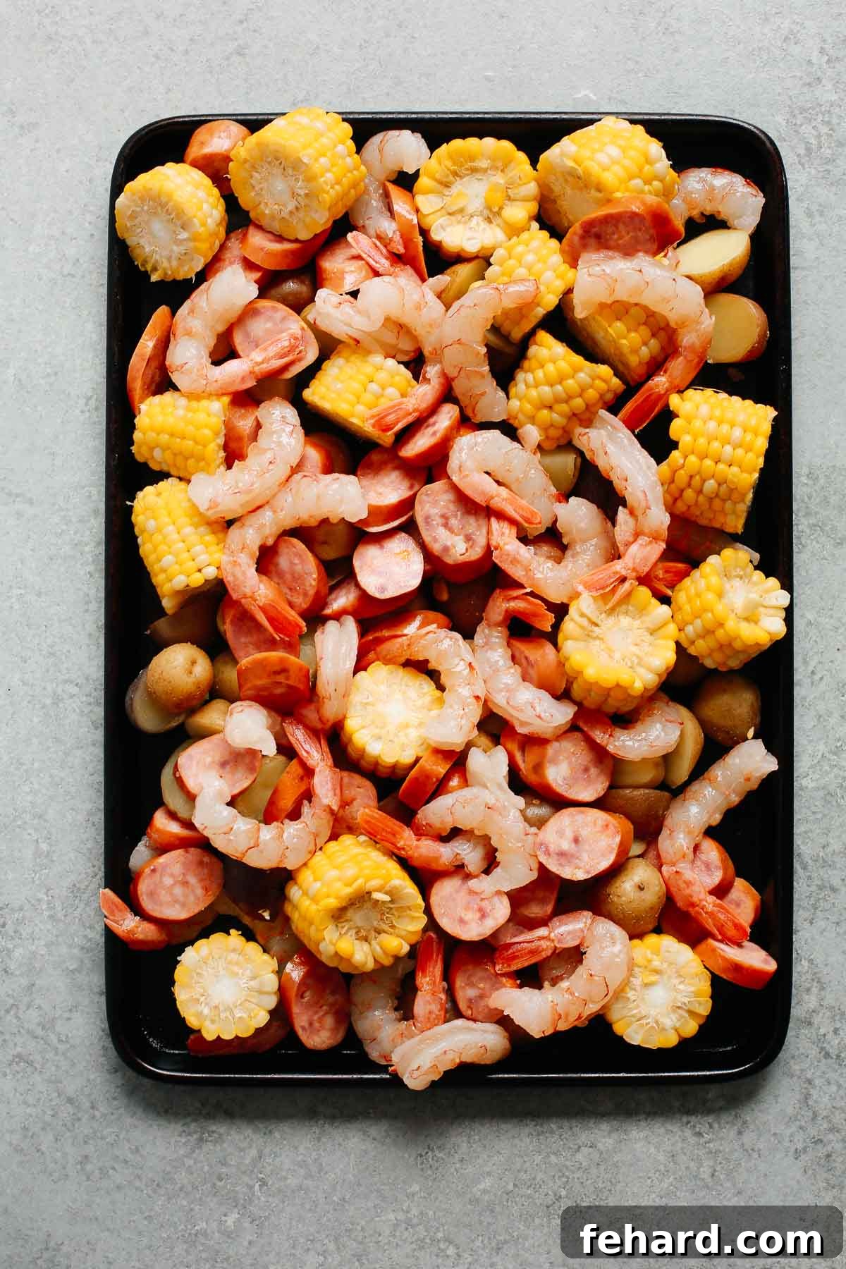 Easy One Pan Shrimp Boil 3 baking sheet with shrimp, sausage, corn, and potatoes before baking, showing the colorful arrangement of fresh ingredients