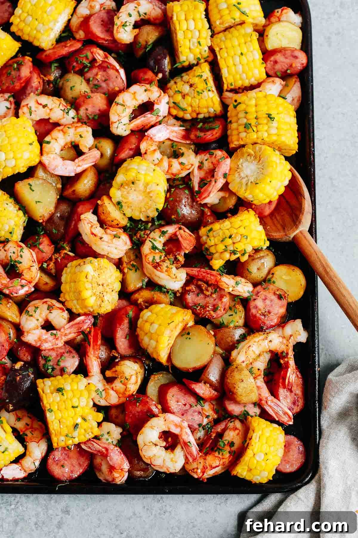 Easy One Pan Shrimp Boil 6 cooked shrimp dinner on a sheet pan with wooden spoon, ready to be served