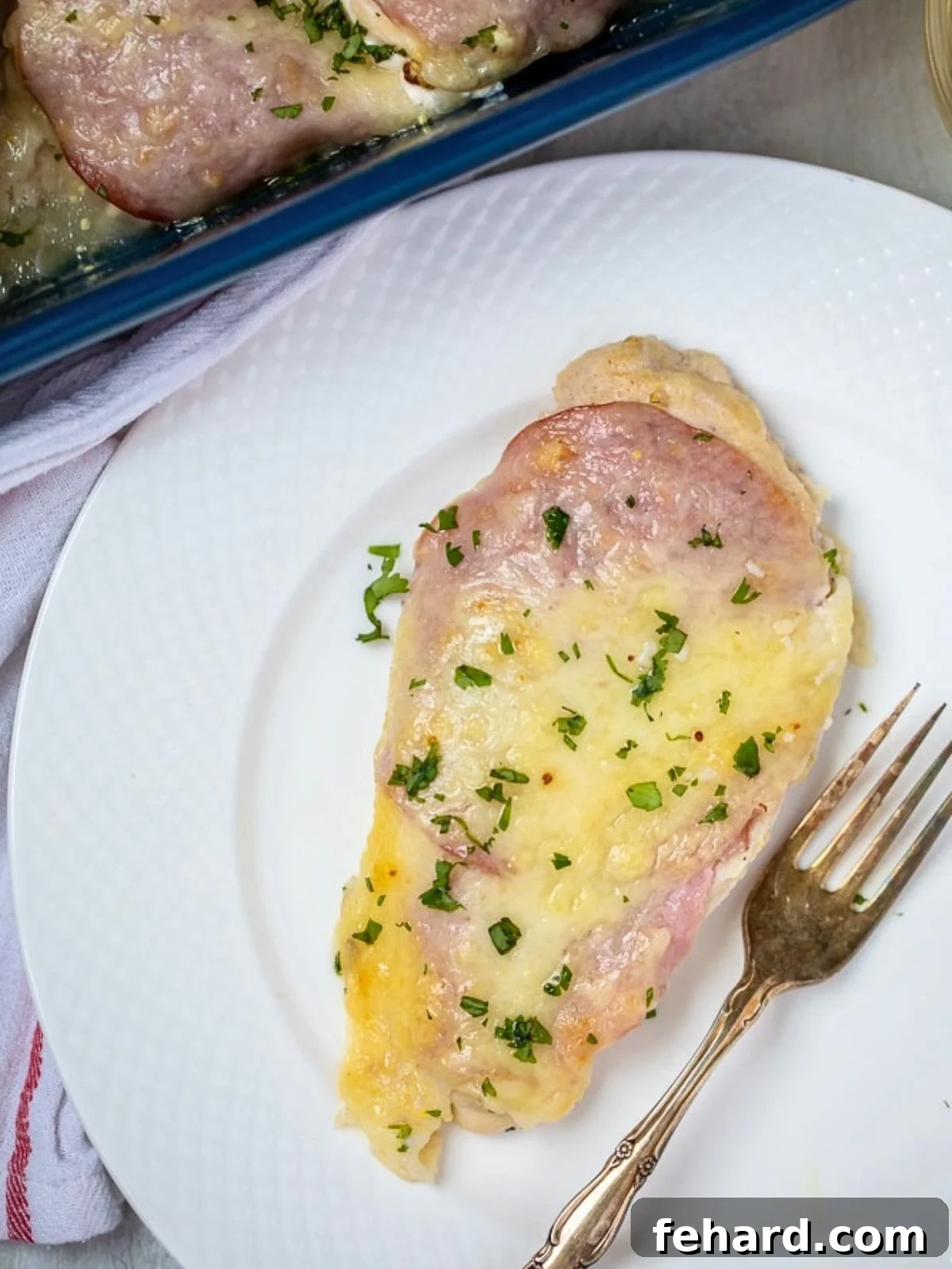 Chicken cordon bleu without breading baked and served on white plate topped with parsley.