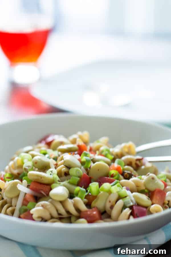 close up of pasta salad with lima beans and anchovies topped with sliced scallions