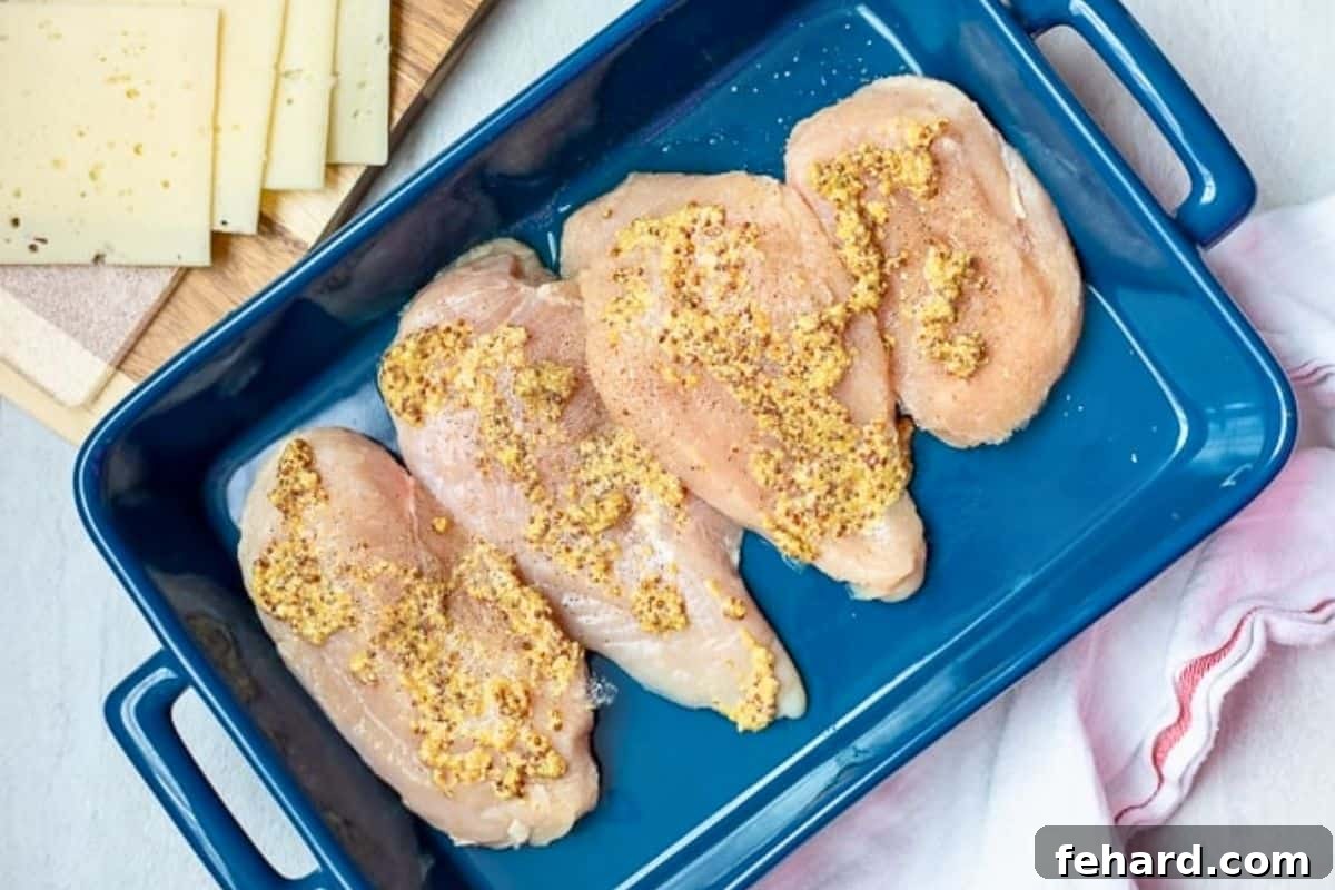 Chicken breasts brushed with Dijon in blue baking dish.