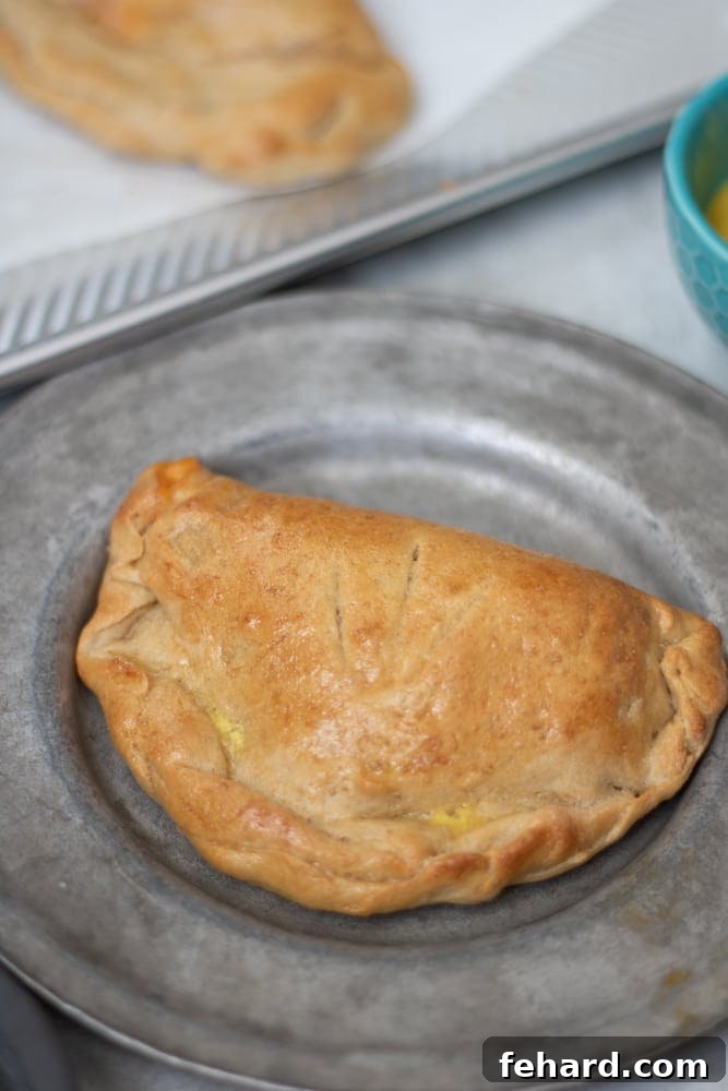Golden brown Homemade Hot Pocket with Ham and Cheese on a plate, surrounded by more hot pockets on a baking sheet.