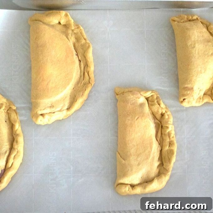 Assembled hot pockets, ready for baking, neatly arranged on a parchment-lined baking sheet.