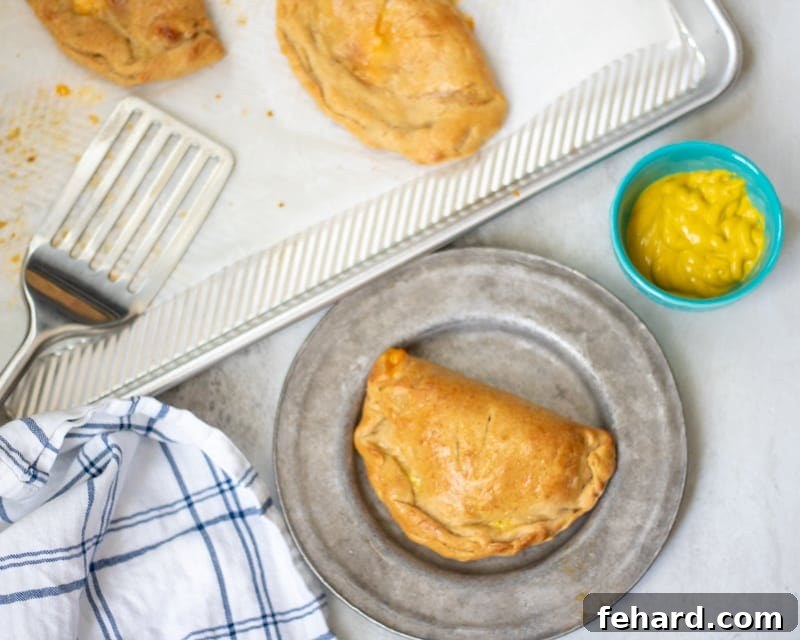 A freshly baked ham and cheese hot pocket, sliced open to reveal gooey cheese, resting on a grey plate next to a pan of other hot pockets.