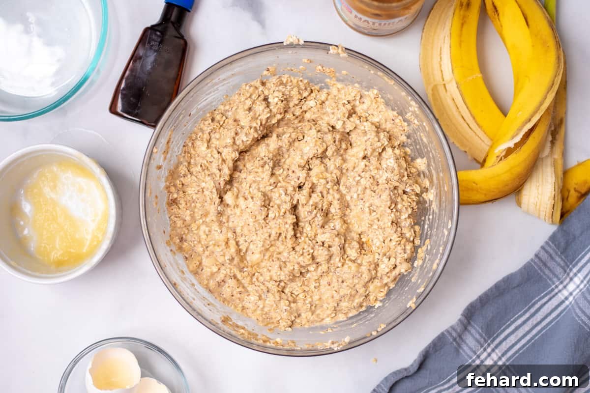A clear mixing bowl filled with the prepared oatmeal cup batter, with banana peels in the background, showing the fresh ingredients used to make dairy-free oatmeal cups.