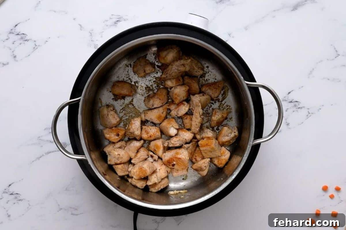 Cubed chicken breasts searing in a stockpot, turning golden brown for flavor in the orzo soup.