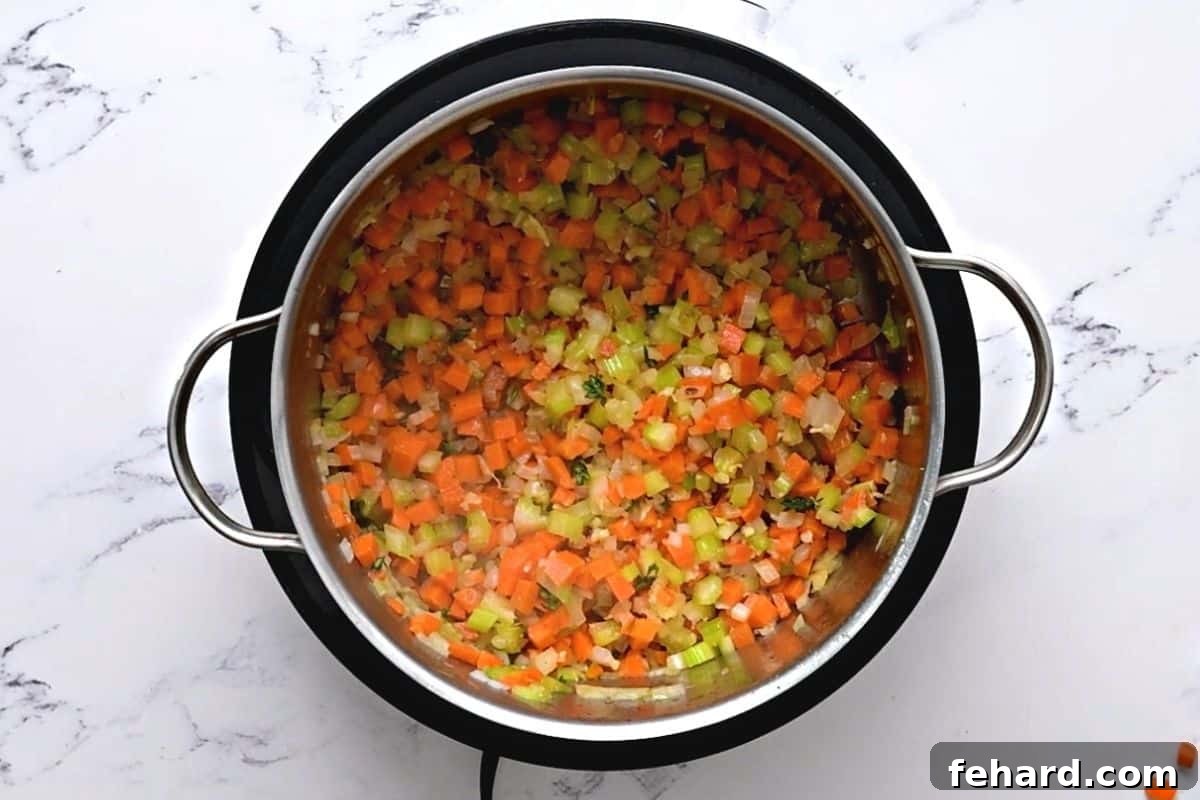 Diced carrots, onions, and celery sautéing in a stockpot, forming the aromatic base for chicken orzo soup.
