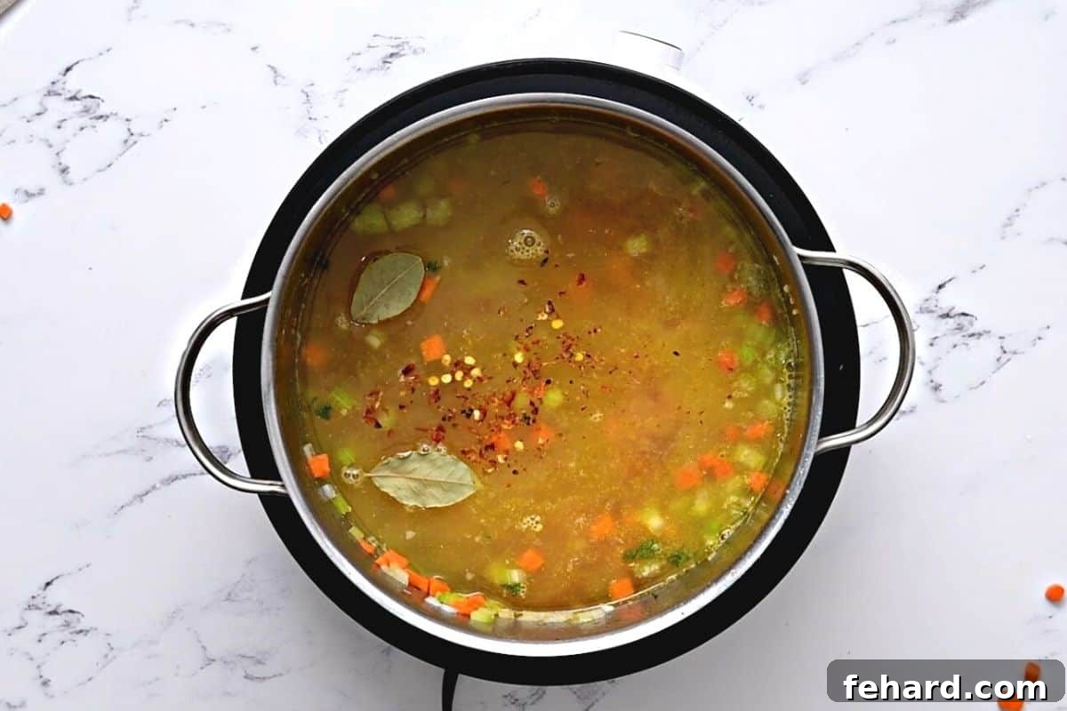 Chicken broth simmering with sautéed vegetables and bay leaves in a stockpot, creating a rich base for lemon orzo soup.