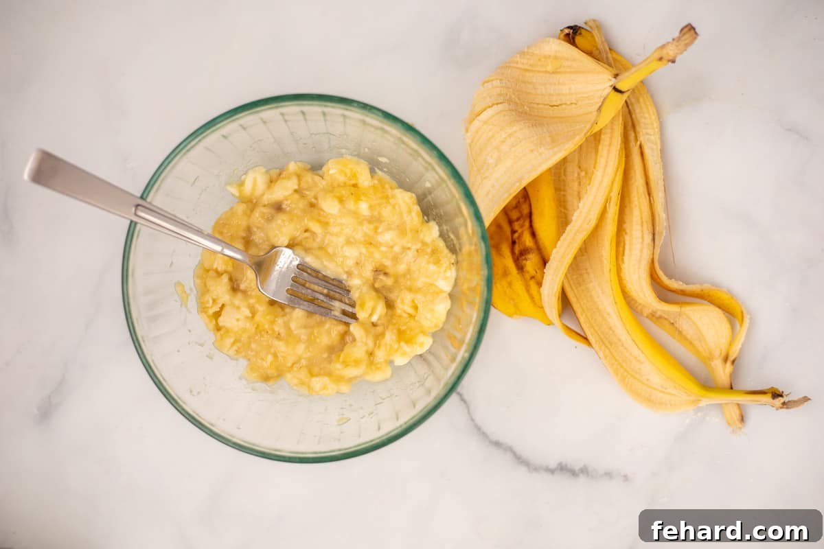 Bowl with mashed bananas next to banana peels, ready for mixing.