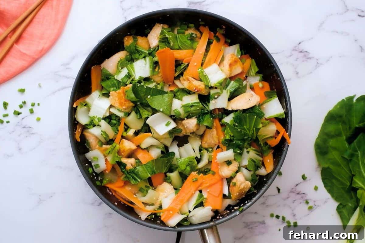 Colorful assortment of chopped bok choy, delicate carrot ribbons, and fresh green onions being added to the pan with browned chicken for an easy stir-fry.