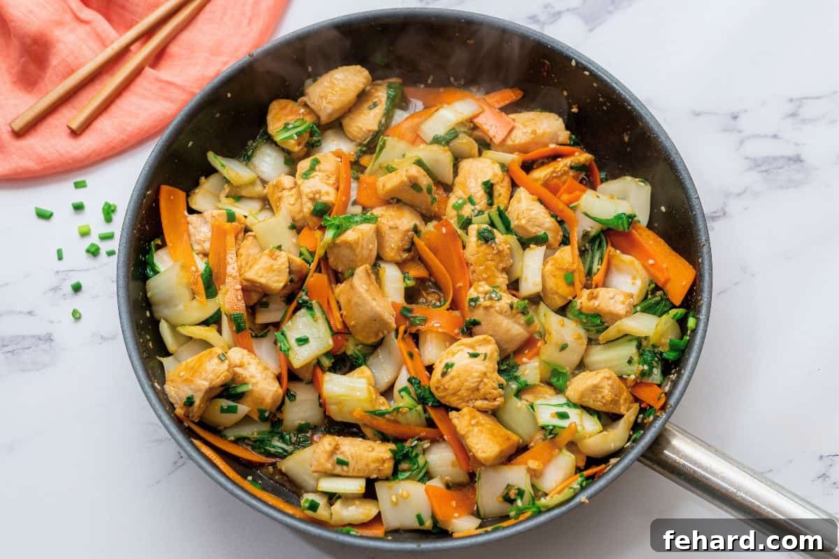 The finished chicken, bok choy, and carrots are tossed generously with a rich soy honey sauce in a large skillet, ready to be served.