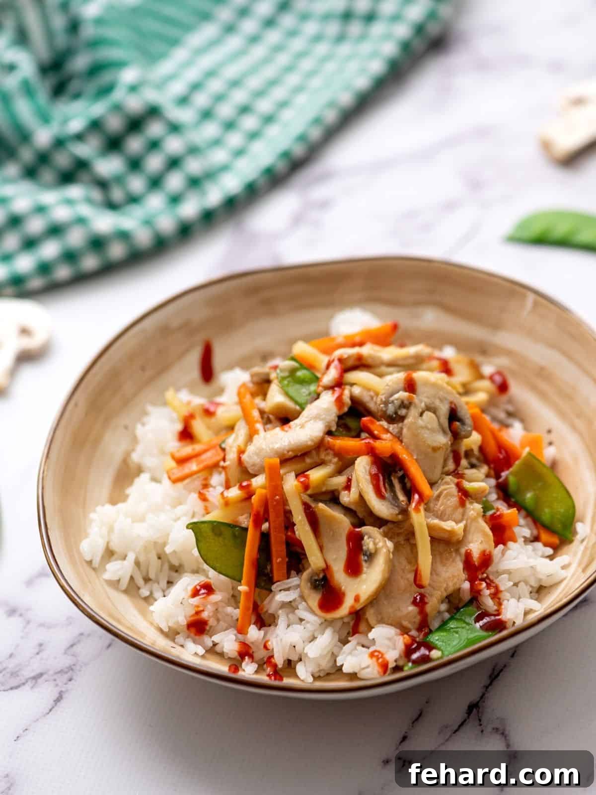 Moo Goo Gai Pan served on top of fluffy white rice, garnished with fresh green onions and a drizzle of hot sauce, highlighting the tender chicken, sliced mushrooms, and vibrant vegetables in a glossy, appetizing sauce.