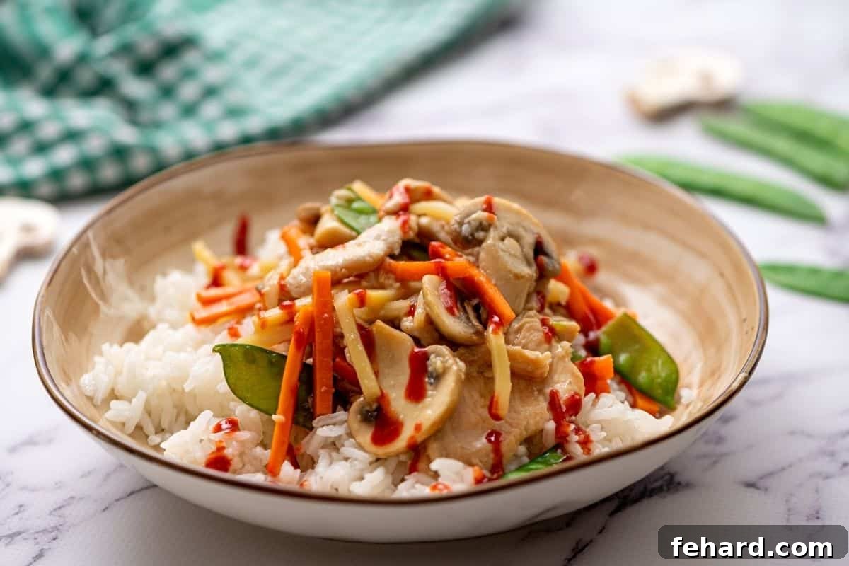 A beautifully presented bowl of Moo Goo Gai Pan, featuring tender chicken, mushrooms, and vibrant vegetables, served over rice with a side of hot sauce for customization.