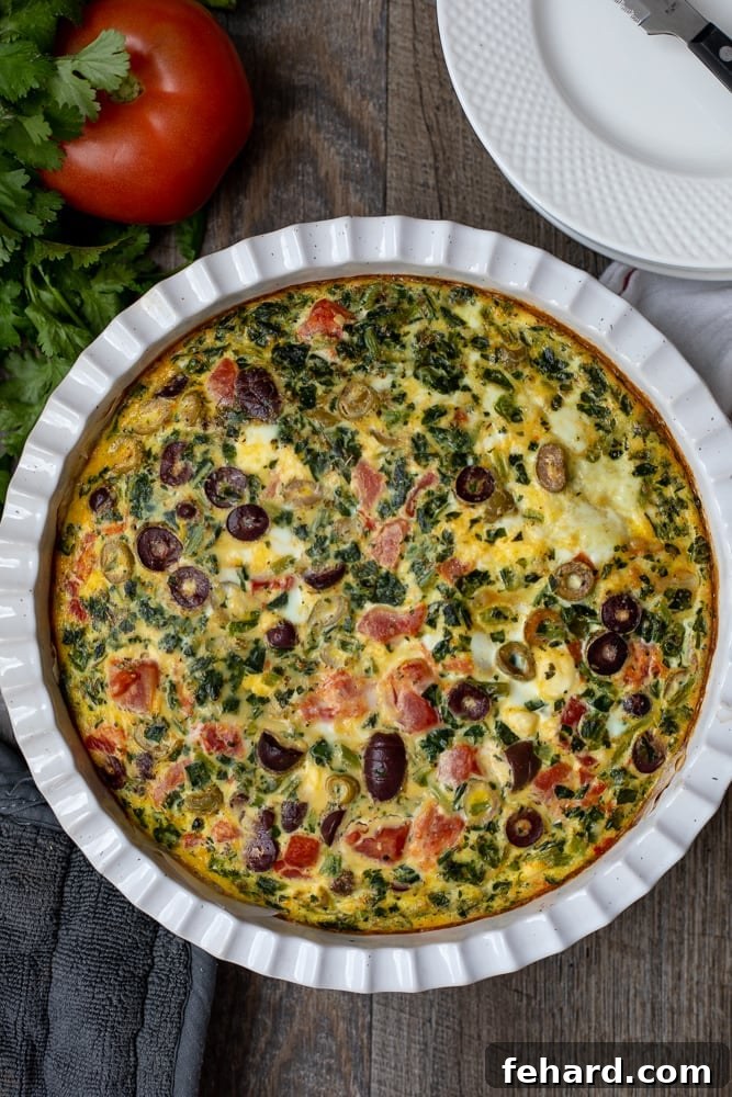 Vibrant Mediterranean Spinach Frittata in a white ceramic quiche dish, garnished with fresh tomatoes, ready to be served. A healthy and flavorful brunch option.