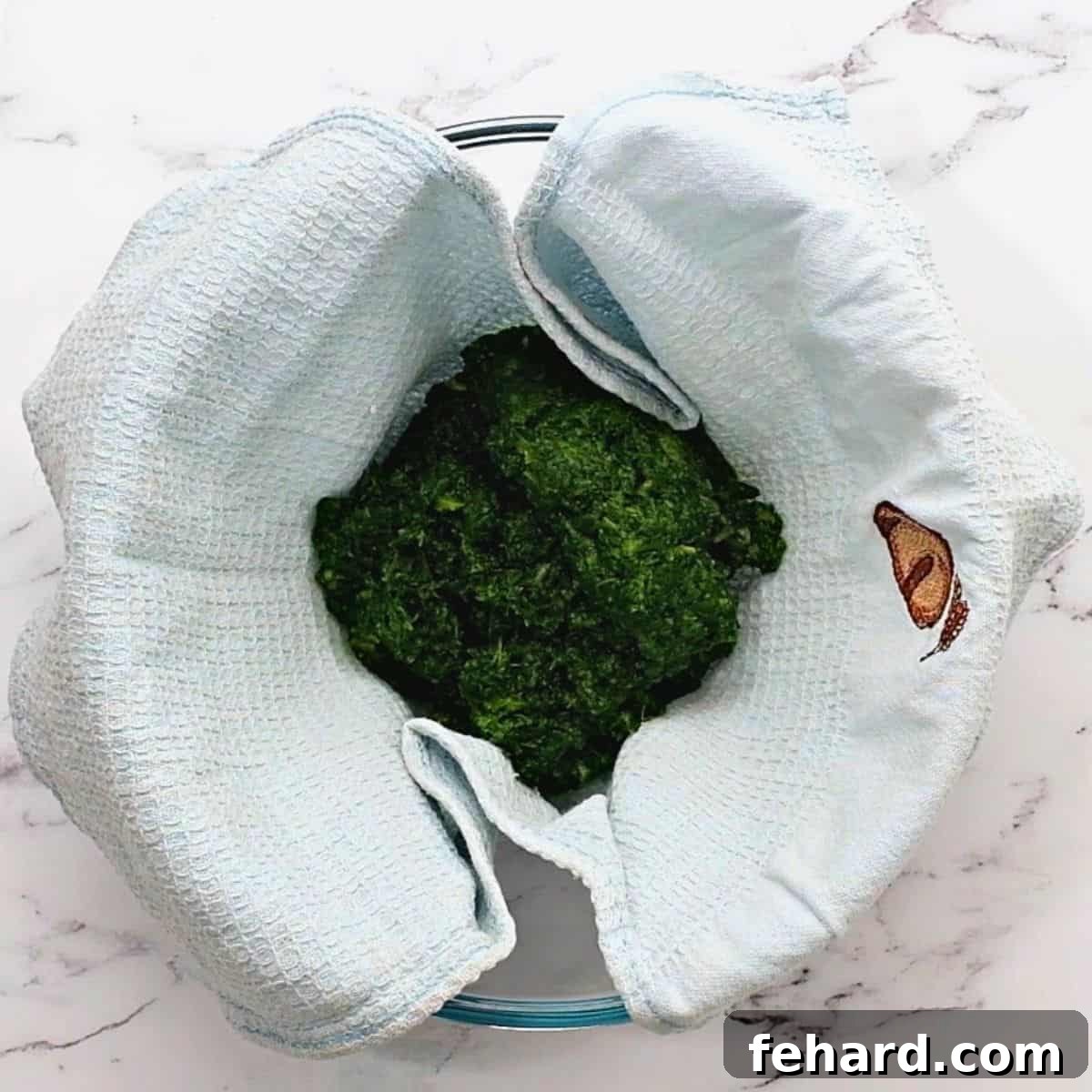Defrosted frozen spinach being squeezed dry in a clean kitchen towel to remove excess water for the frittata.