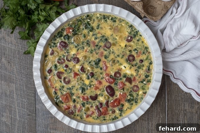 Mediterranean Frittata mixture poured into a greased baking dish, showcasing colorful ingredients before baking.
