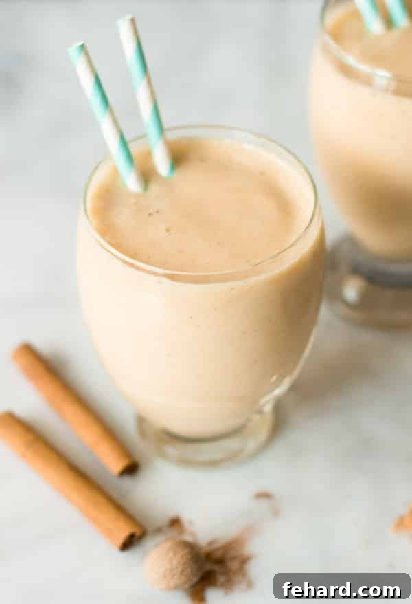 Glass cup of vibrant Spicy Pineapple Peach Smoothie with straws inserted, garnished with fresh mint and a peach slice.