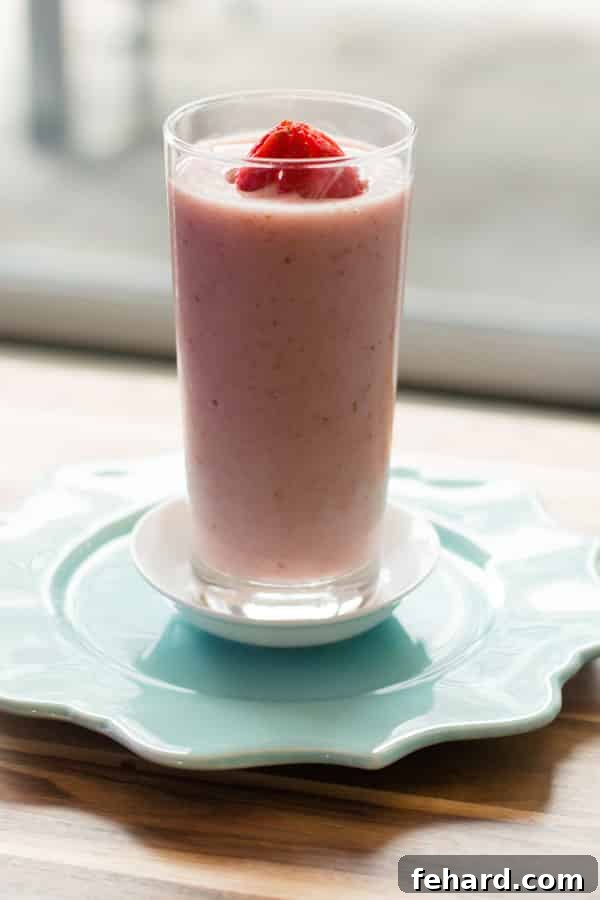 Strawberry and papaya smoothie in a clear glass, garnished with a fresh strawberry on top, showcasing its vibrant, appealing colors.