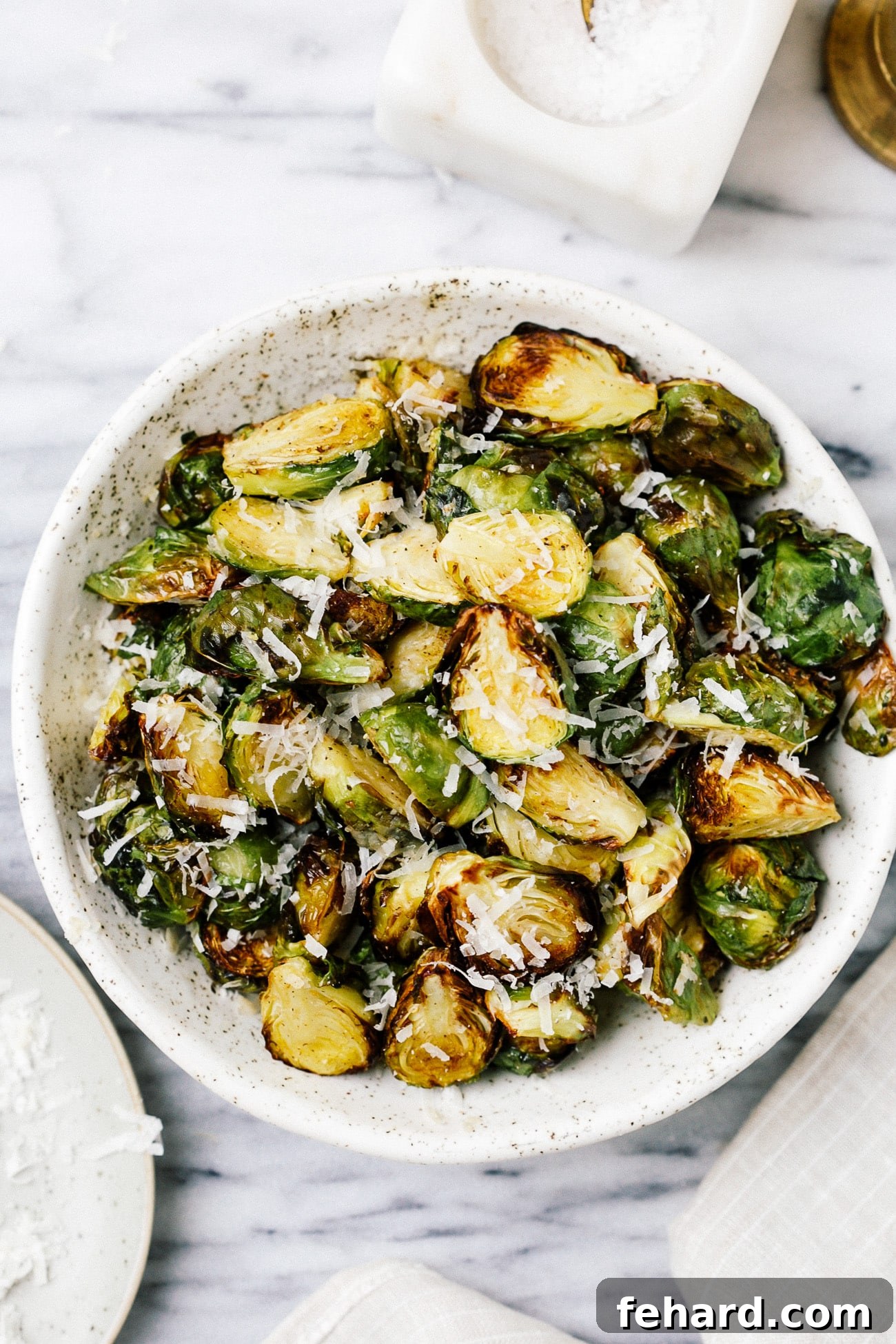 A serving bowl full of crispy Brussels sprouts topped with parmesan cheese. 