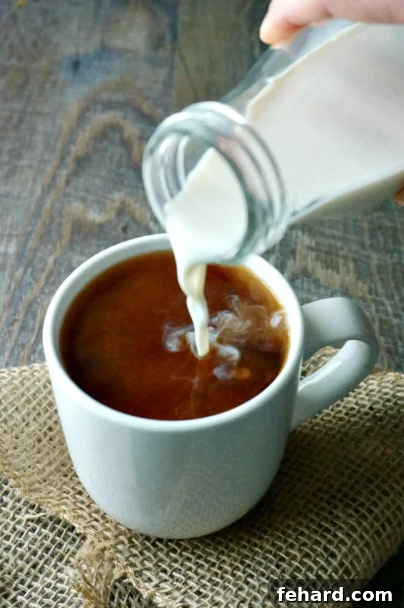 Homemade Coconut Vanilla Coffee Creamer being poured into a coffee cup, highlighting its smooth, creamy texture and rich white color against the dark coffee.