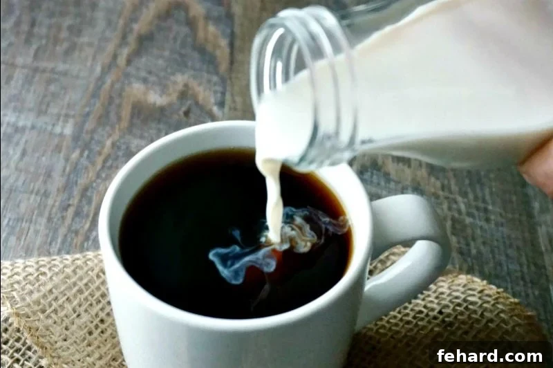 Vanilla Coconut Coffee Creamer being poured into dark coffee in a clear glass mug, creating beautiful swirling patterns as it mixes.