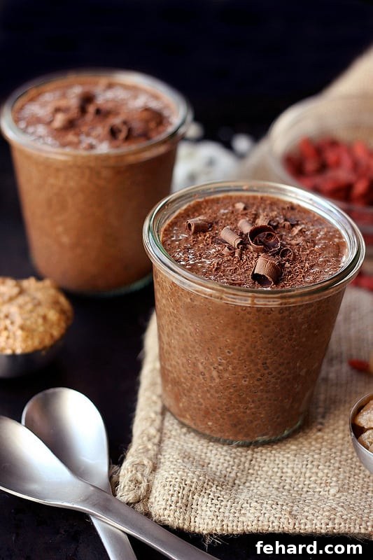 Two elegant glass cups containing creamy chocolate chia seed superfood pudding, garnished with a sprinkle of cocoa powder, with two spoons invitingly placed beside them.