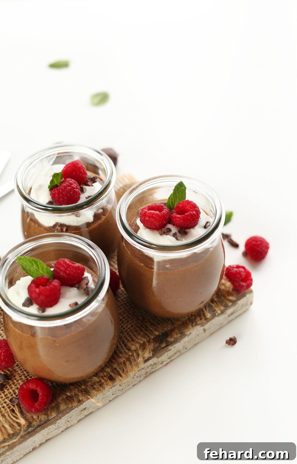 Three individual servings of luscious overnight chocolate chia seed pudding, artfully garnished with fresh raspberries, vibrant mint leaves, chocolate chips, and a dollop of whipped cream.