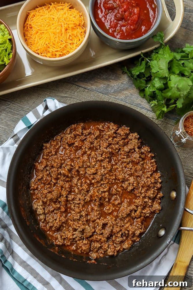 Flavorful homemade taco meat simmering in a skillet, surrounded by fresh ingredients for tacos like lettuce, tomatoes, cheese, and tortillas.