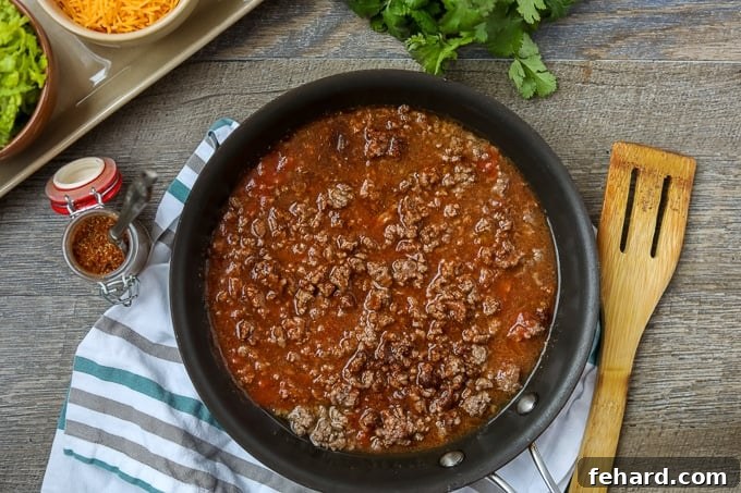 Tomato sauce, water, and homemade taco seasoning added to browned ground beef in a skillet.