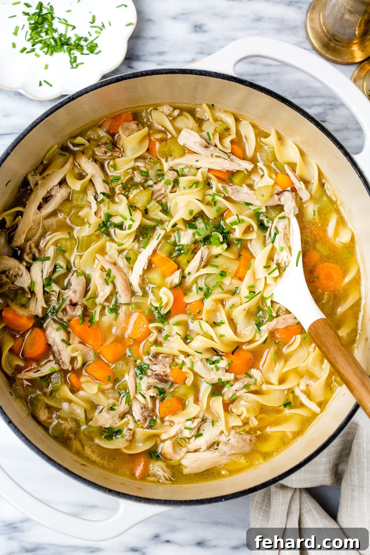 Chicken noodle soup in a large white pot.