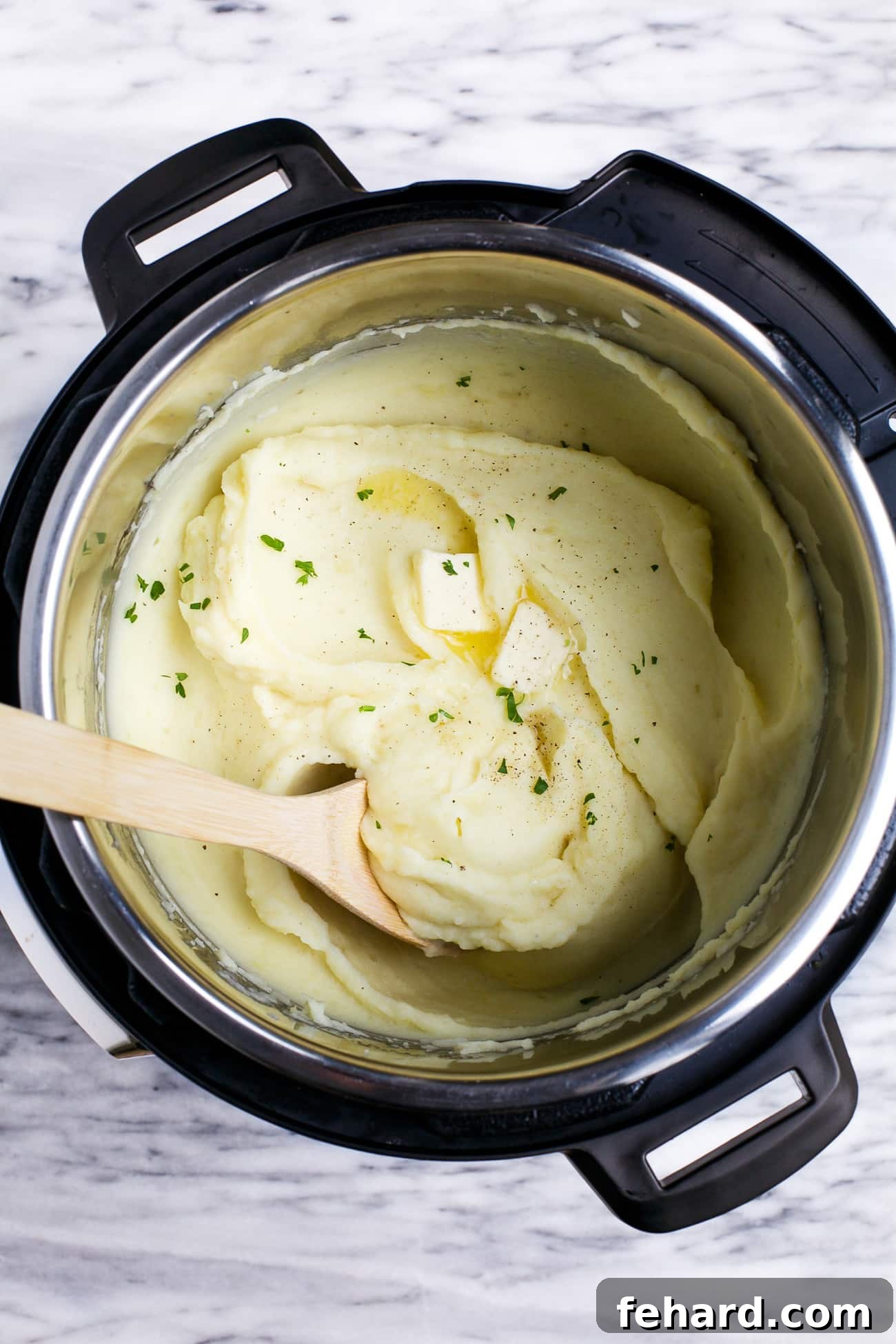 A bowl of finished Instant Pot mashed potatoes, topped with a dollop of butter and fresh parsley.