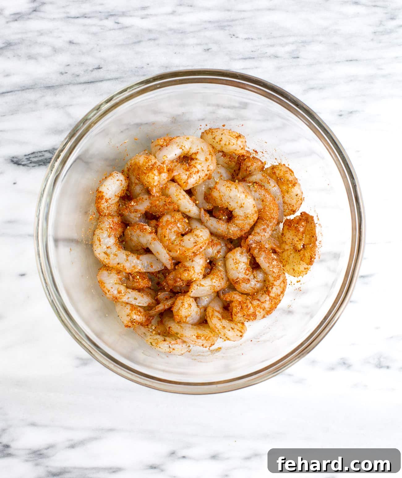 seasoned raw shrimp in a glass bowl ready to be skewered