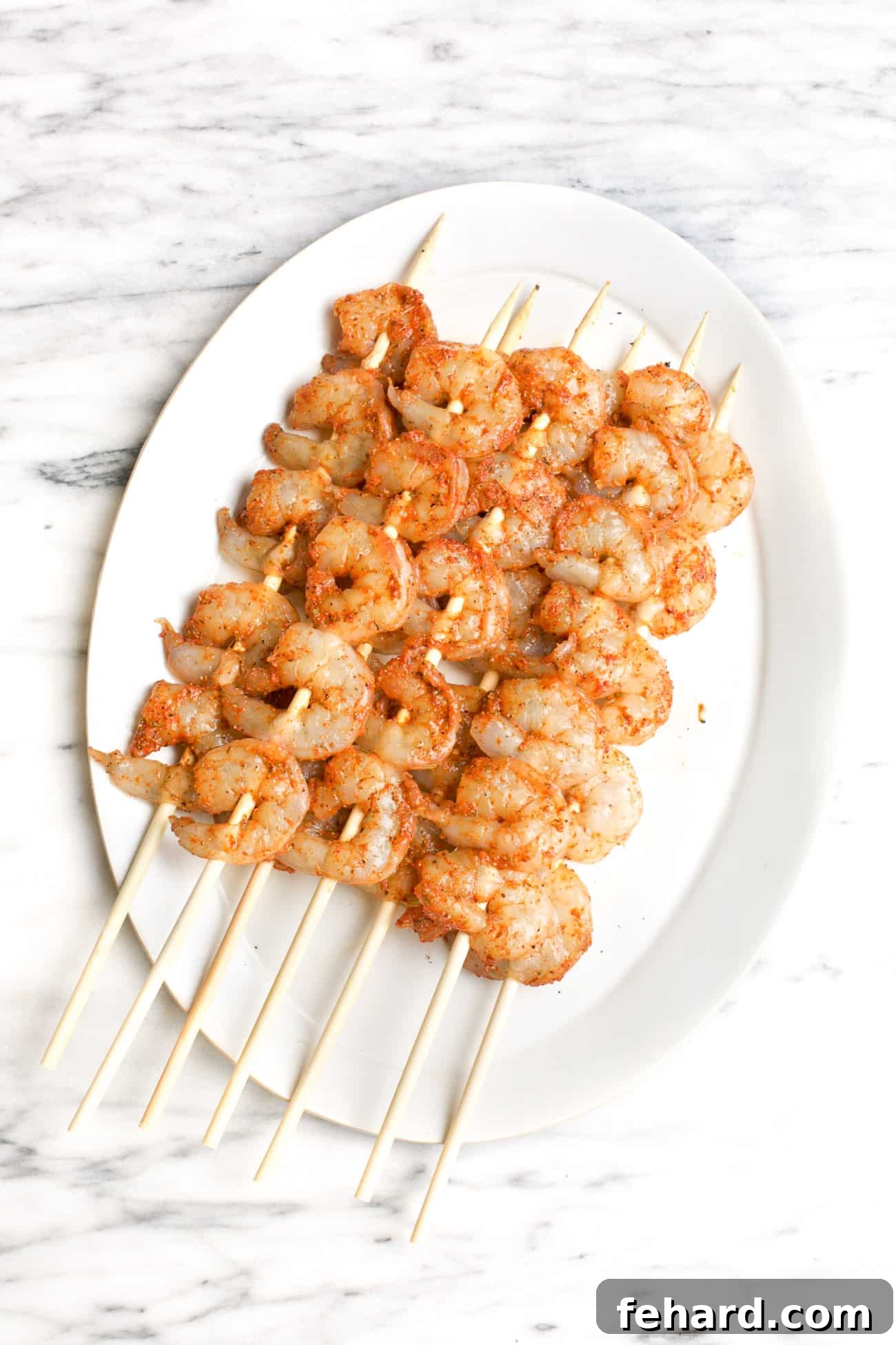 raw seasoned shrimp skewered on wooden sticks on a white plate
