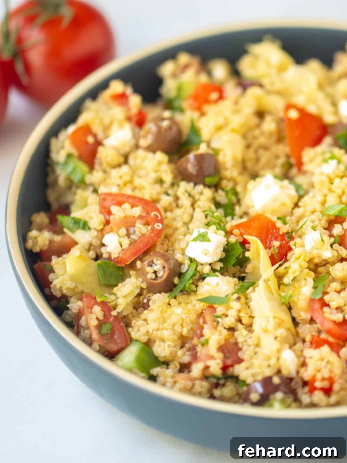 Greek Quinoa Salad Bowl of Greek Quinoa Salad with fresh parsley, surrounded by ripe tomatoes and olives.