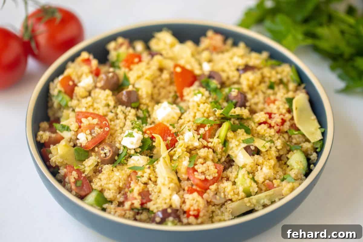 Mediterranean Quinoa Salad Recipe Prepared Quinoa Salad in a blue bowl, garnished with olives, feta, and tomatoes, ready to serve.