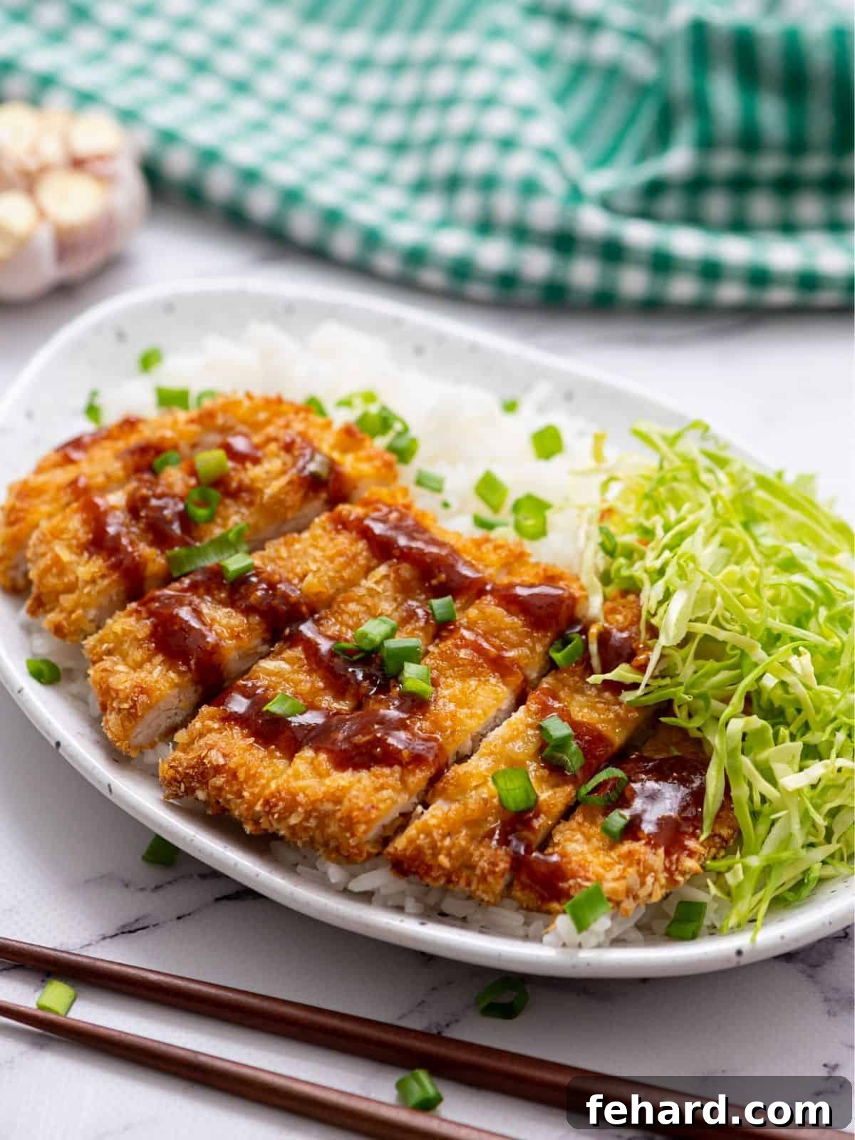 Sliced Baked Chicken Katsu served on a plate with fluffy white rice and a side of fresh shredded cabbage, garnished with green onions.