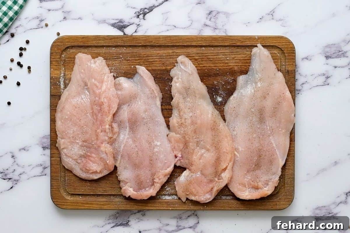 Four pounded chicken cutlets laid out on a cutting board, ready for breading.